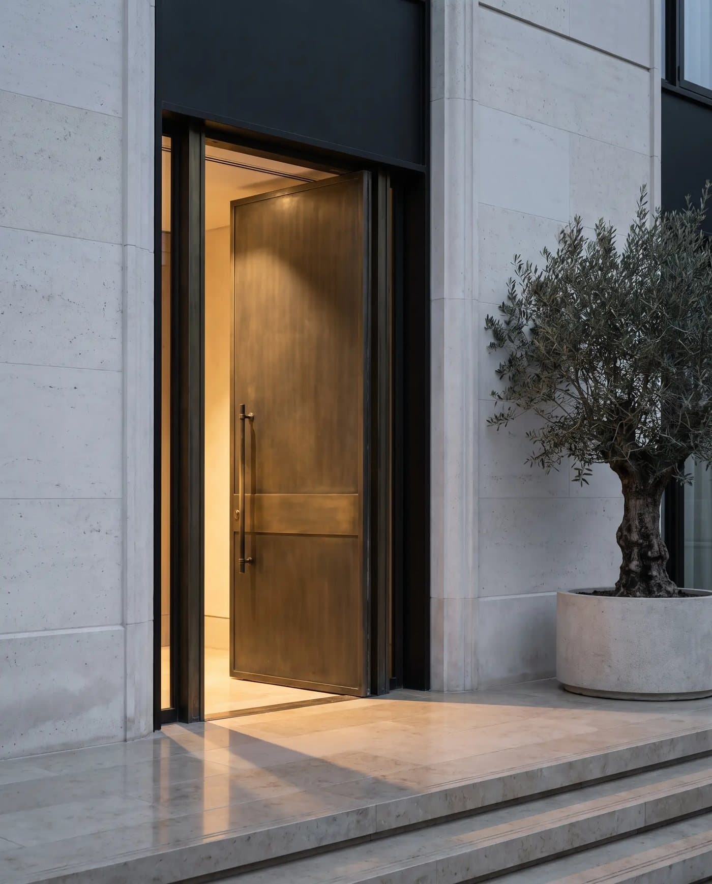 A bronze door standing ajar in a pale stone facade at dusk